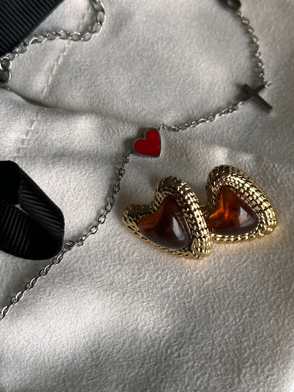 Gold heart-shaped earrings with red stones on a textured surface