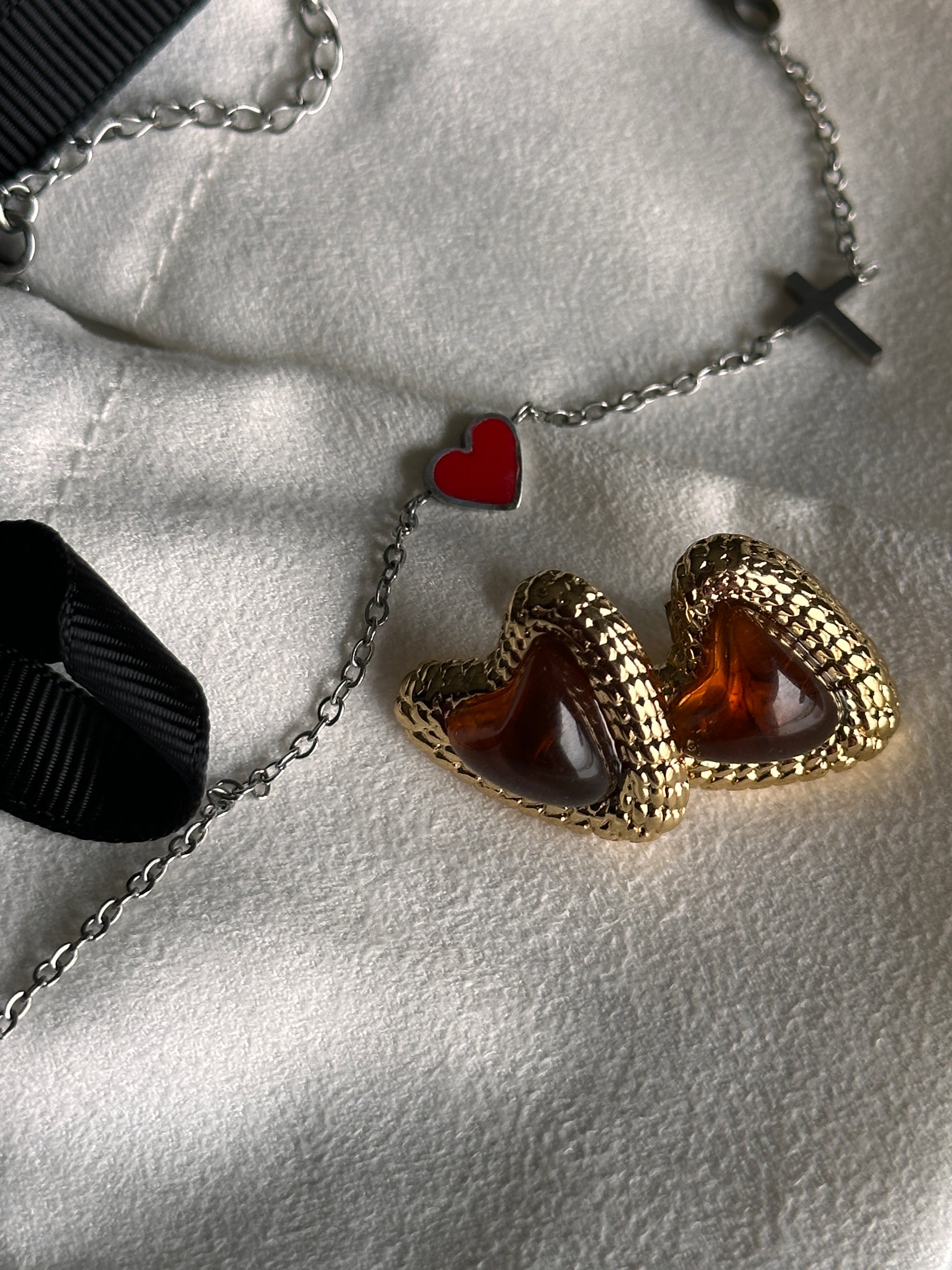 Gold heart-shaped earrings with red stones on a textured surface