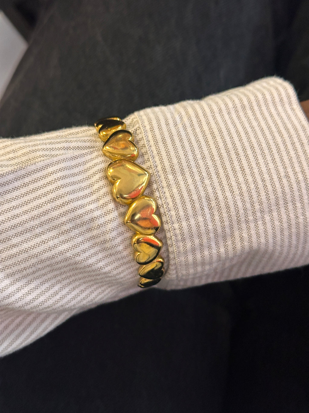 Gold bracelet with heart-shaped charms on a wrist against a dark background