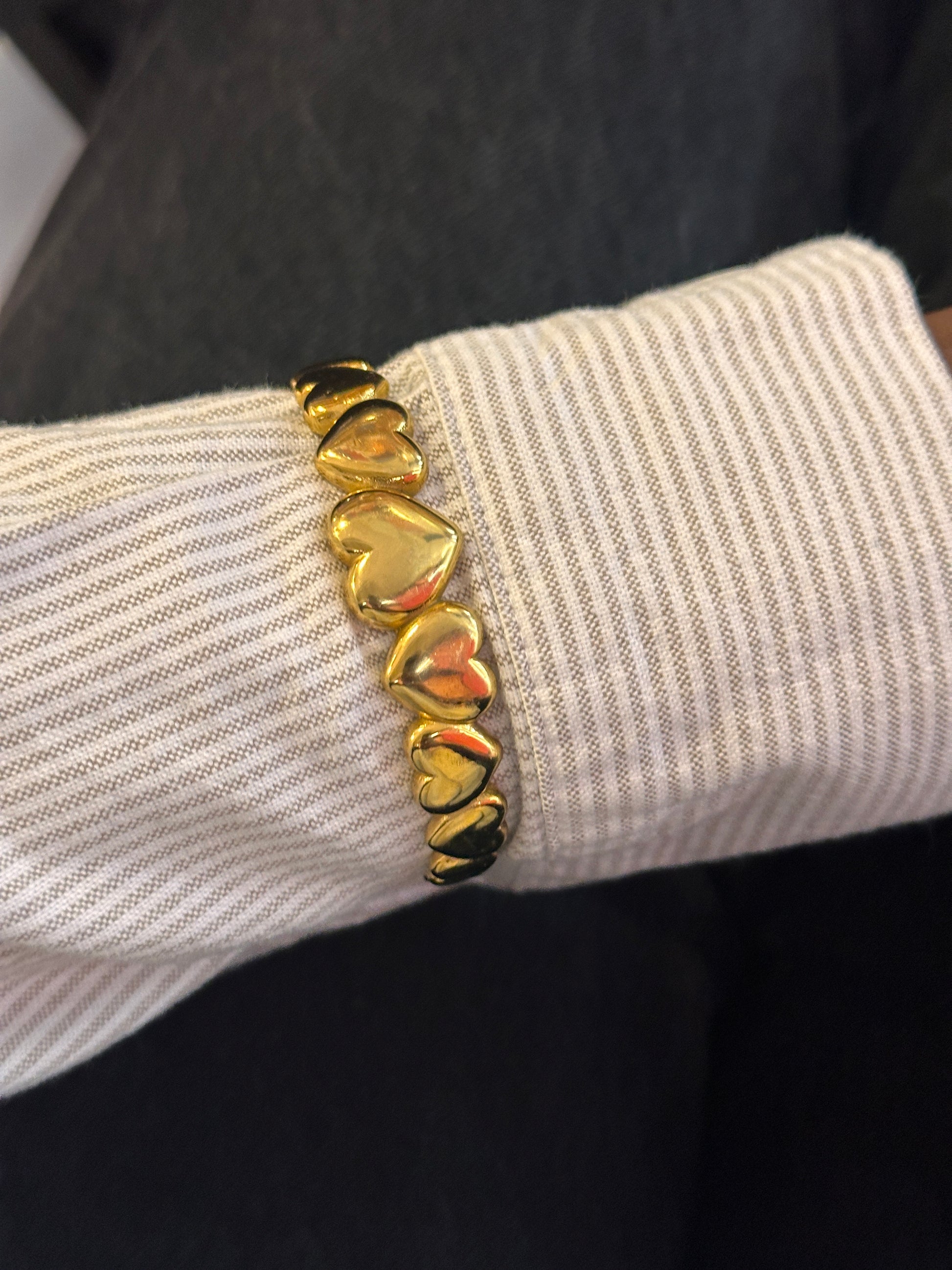 Gold bracelet with heart-shaped charms on a wrist against a dark background