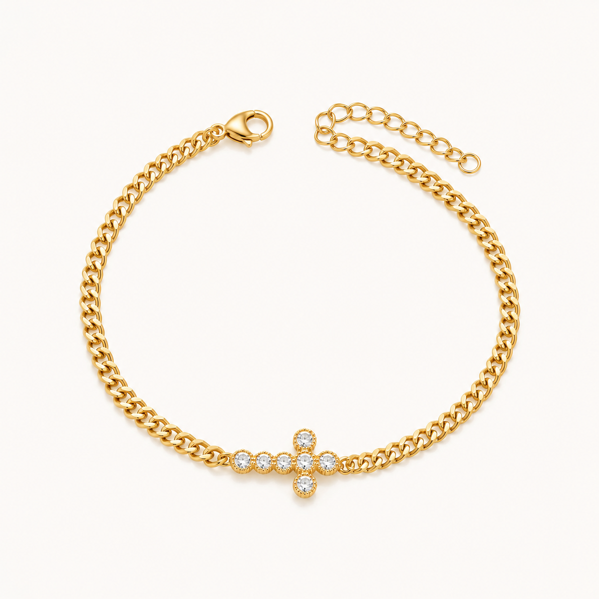 A gold chain bracelet with a central cross charm paved with clear stones, displayed on a clean off-white background.
