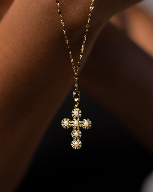 Close-up shot of a gold and silver cross necklace adorned with delicate pearls, symbolizing the juxtaposition of the King of Kings dying a lowly death. This beauty cross necklace, inspired by Philippians 2:8 ('He humbled himself by becoming obedient to death—even death on a cross'), is a meaningful gift for baptisms or Easter, blending elegance with profound spiritual significance.