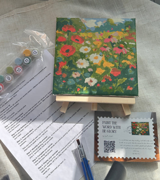 Small floral painting on an easel with art supplies and a postcard on a textured surface