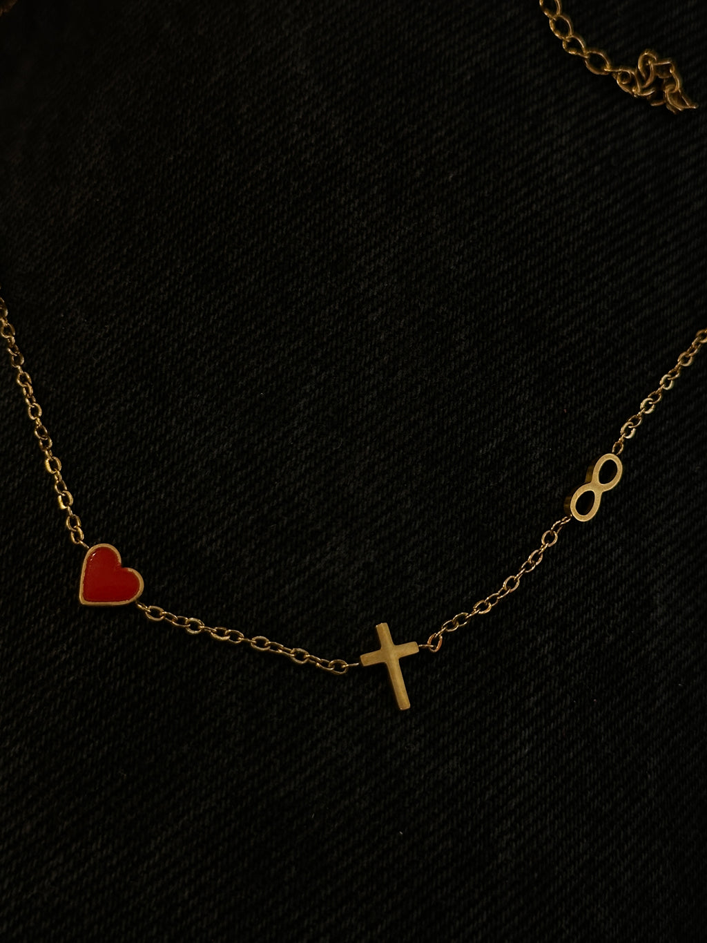 Gold chain bracelet with a red heart and cross on a black background